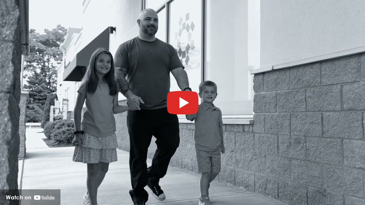 Adult walking outdoors with two children along a sidewalk near a medical building